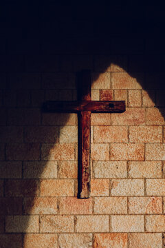 Wooden cross on brick wall in dramatic sunlight