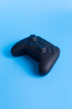 Vertical angled view of black wireless gamepad controller on blue background. Minimalist design for social media gaming and esports ads.
