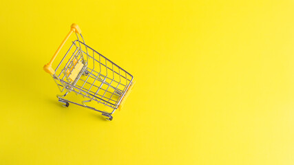 Top view of yellow miniature shopping cart on solid yellow background with copy space. Concept for retail ecommerce and online shopping.  © wibiwisnu