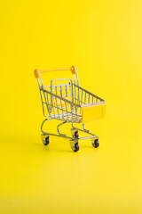 Angled yellow miniature shopping cart on solid yellow background. Vertical social media concept for ecommerce retail and online shopping.  © wibiwisnu