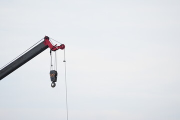 Crane hook suspended from a lifting boom against the sky, representing construction machinery, rigging equipment, heavy lifting and industrial operations © belavinstock