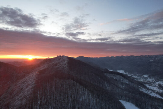 Aerial view of stunning dramatic sunrise over winter mountain ridge, drone shot of sun rising behind snowy hills and forest in cold morning twilight, beautiful majestic nature landscape, carpathians