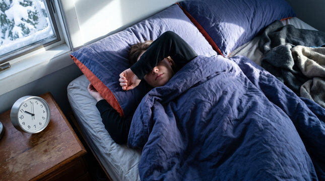 Young man sleeping in bed under blankets during winter morning  