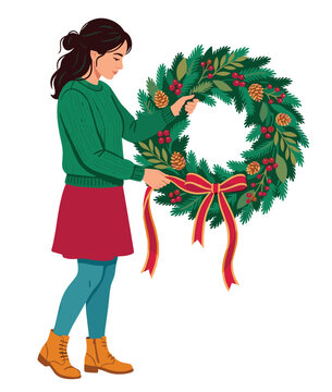 Young woman carefully decorates a beautiful festive Christmas wreath adorned with pinecones and red berries for the holiday season.