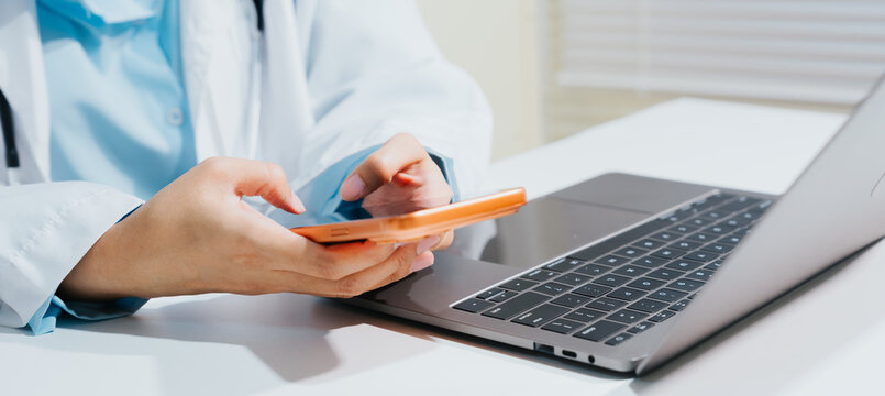 Professional doctor using smartphone and laptop device for medical research while feeling concentrated and focused in office environment