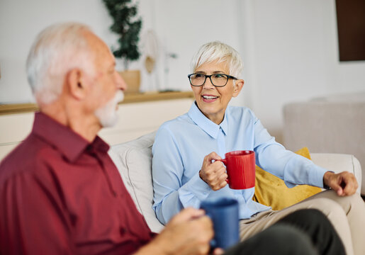 Portrait of a happy senior couple embracing talking and drinking coffee or tea at home