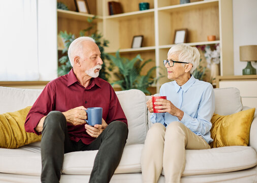 Portrait of a happy senior couple embracing talking and drinking coffee or tea at home