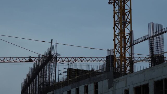 Tower crane and steel rebar rising above a reinforced concrete structure, showing high rise construction, structural engineering and urban development