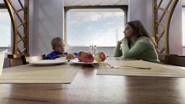 A mother and son sit together at a table inside a cruise ship on the Neva River in Saint Petersburg. This cozy moment creates warm, happy, and peaceful feelings during their pleasant journey.