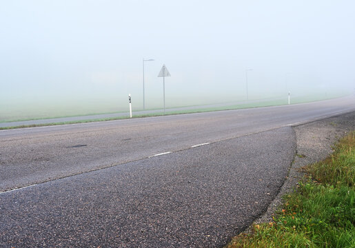 An empty rural road disappearing into dense fog on a quiet morning