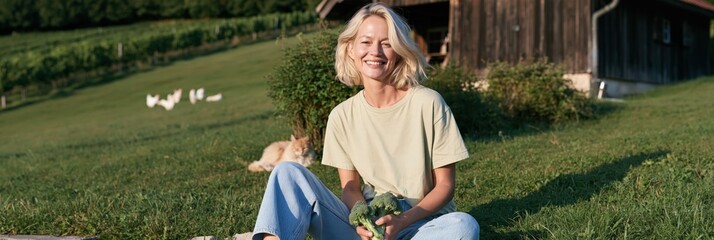 Fototapeta premium Woman sitting on a sunny hillside holding fresh vegetables for rural farm lifestyle background and sustainable living banner