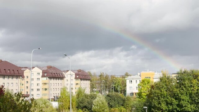 A bright rainbow arcs gracefully above apartment buildings in Pushkin, Saint Petersburg. The colorful view brings a serene sense of awe and hope to the quiet neighborhood.
