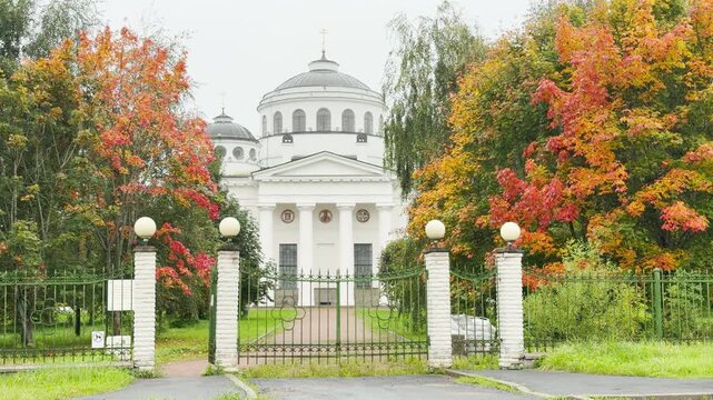 Saint Sophia Cathedral stands serenely behind a green gate. Vibrant autumn trees frame the quiet path in Pushkin, Saint Petersburg, creating a peaceful and inspiring atmosphere.