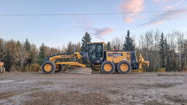 CALGARY, CANADA - 26 SEPTEMBER 2026: Yellow Komatsu GD655 motor grader heavy machinery parked on dirt road in Alberta Canada