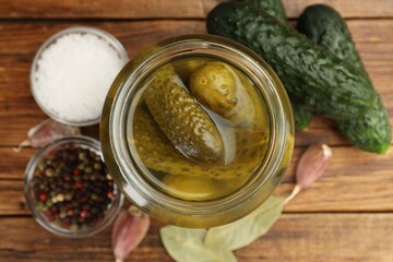 Fototapeta premium Pickled cucumbers in glass jar, fresh vegetables and spices on wooden table, flat lay