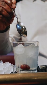 Vertical video: Tilting whiteclad server holding spoon, cherry after syrup, garnishing drink at bar