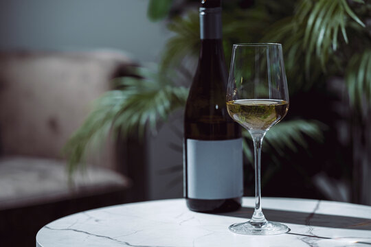 Dry white wine in glass beside bottle on white marble table, healthy heart lifestyle choice. Non-alcoholic dealcoholized Sauvignon Blanc drink. Sober wellness and longevity concept.