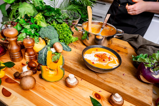 Homemade autumn food &mdash; woman preparing comfort pumpkin soup. Healthy eating concept and domestic culinary lifestyle. Female hands over wooden table with organic vegetarian meal in dark ceramic bowl.