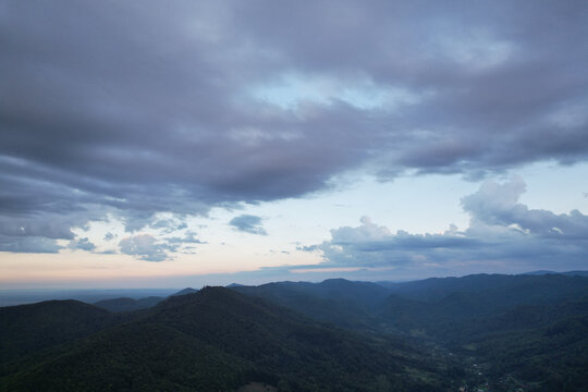 Aerial view of majestic twilight over green mountain ranges and valleys under cloudy sky, drone panoramic shot of mountains silhouettes at evening dusk, scenic countryside background, carpathians 