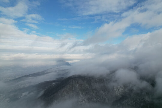 Aerial view of winter mountains with low clouds and thick fog rolling over forest slopes, drone panoramic shot of flying above valley in misty weather, scenic overcast landscape, carpathians