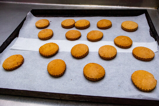 round golden-colored butter cookies pulled out of the oven, baking sheet, parchment for baking, wavy edge, 