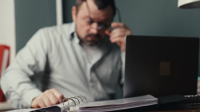Exhausted male freelancer rubbing eyes from laptop screen fatigue at night