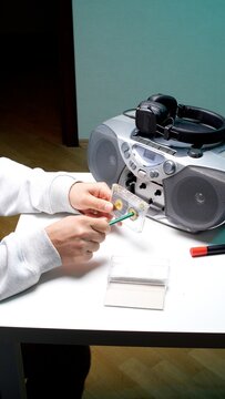 Person using a pencil to manually rewind an old audio cassette tape on a white table next to a vintage boombox and headphones, symbolizing nostalgia for past decades and music technology