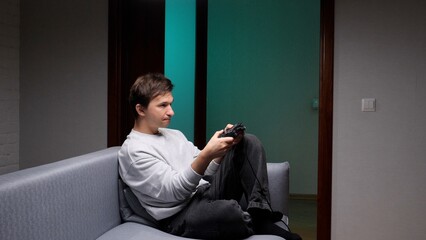 Young man on a modern couch intently playing video games with a controller, focused and relaxed during casual home leisure time in a contemporary living room setting © Aliaksandr