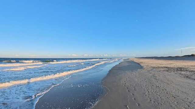  4K beach video reveals rolling waves beyond footprints along a sandy shore.
