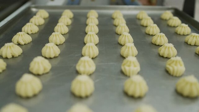 Close up tracking shot of piped cookie dough on a metal baking sheet in a commercial kitchen