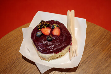 Cinnamon roll topped with dark berry glaze, fresh strawberries and blueberries, served on a wooden table, visible film grain. high quality photo © Татьяна Швец