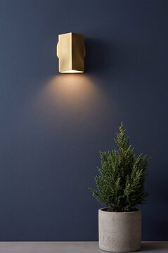 Modern gold wall lamp illuminating a dark blue wall with greenery  