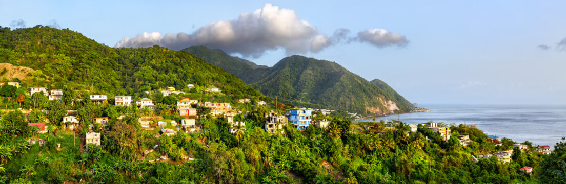 Scenic panoramic view of colorful houses scattered on a lush green tropical hillside overlooking the Caribbean Sea in Dominica