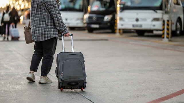 Traveler pulling a rolling suitcase across a bus terminal platform for a journey departure