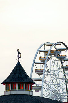 A Ferris wheel next to a cottage in an amusement park with a white sky in the background 