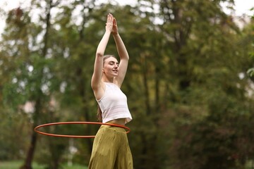Athletic young woman exercising with hula hoop in park, space for text © New Africa