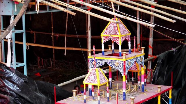 Colorful miniature decorated chariot model with pink and yellow ornaments under bamboo scaffolding, Indian festival decoration