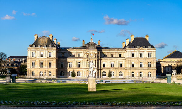 The Luxembourg Palace, the seat of the French Senate with its green lawn and a classic statue under a blue sky in Paris, France.