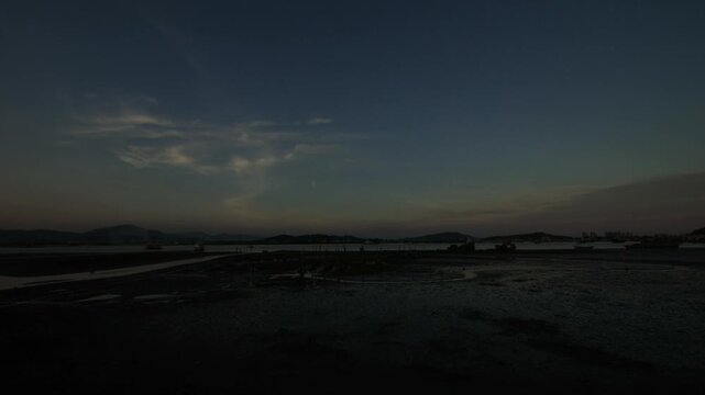 Dusk over coastal mudflats with boats and distant hills at low tide