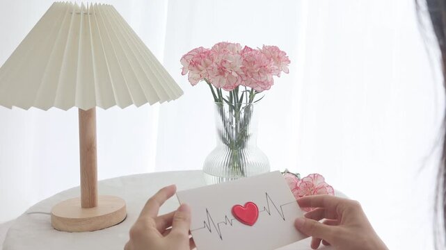 Minimalist interior with pleated lamp and pink carnations in a vase on a white table