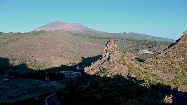 Roque Cinchado rises beside scattered pines with Mount Teide filling the horizon across the volcanic caldera. A sweeping establishing shot of Tenerife's UNESCO World Heritage landscape.