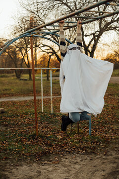 Person wearing ghost costume hanging on monkey bars