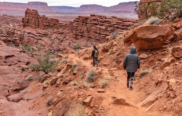 Two hikers walk a red rock trail beneath the sandstone spires of Fisher Towers near Moab, Utah, USA © Katrin