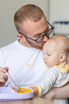 Father kisses his little son while feeding. Father and his baby getting dirty while eating.