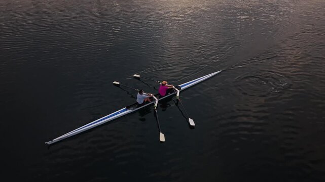 Cinematic aerial view of athletes practicing rowing in Halifax, Nova Scotia, with synchronized oars cutting through the harbour water as the first sunlight appears over the city.