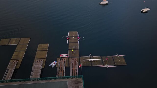 Aerial view of rowing athletes finishing their morning training in Halifax, Nova Scotia, as they dock at a wooden pier and pull their racing boats out of the water.