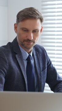 Focused businessman sitting at a modern desk, working intently on a laptop surrounded by folders, showcasing professionalism and determination. Audit and taxes in business