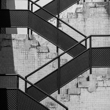 Monochrome industrial fire escape stairs crossing weathered tiled walls. 