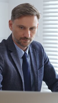 Focused businessman sitting at a modern desk, working intently on a laptop surrounded by folders, showcasing professionalism and determination. Audit and taxes in business