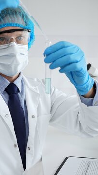 Scientist in protective gear analyzing a test tube of turquoise liquid with a pipette in a modern laboratory setting. Medicine, health care and science concept